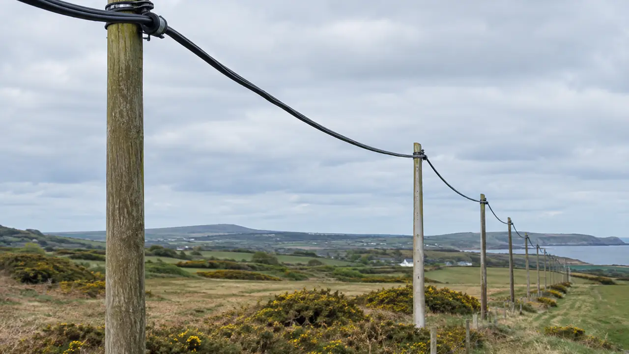 Black ADSS aerial fibre cable strung between wooden utility poles along a rural power line route